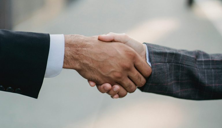 Two businessmen shaking hands outside, symbolizing cooperation and agreement in a city setting.